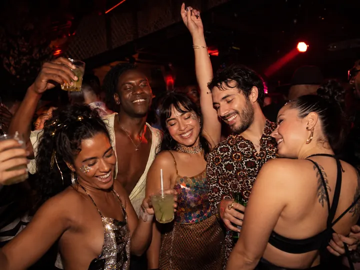 Friends dancing with drinks raised in a warm-lit Rio bar at night